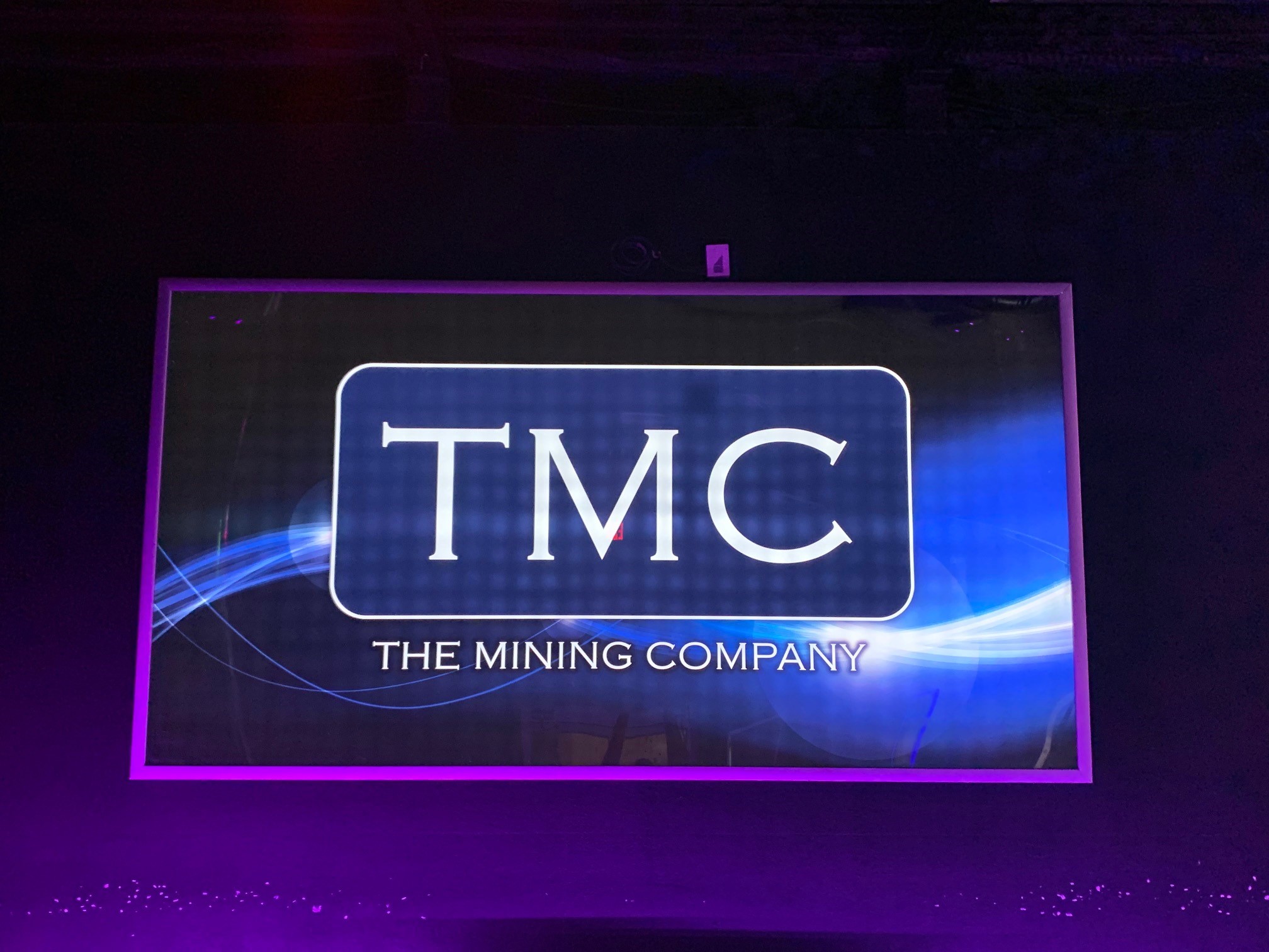 The backlit TMC sign reading The Mining Company glowing in purple and blue neon